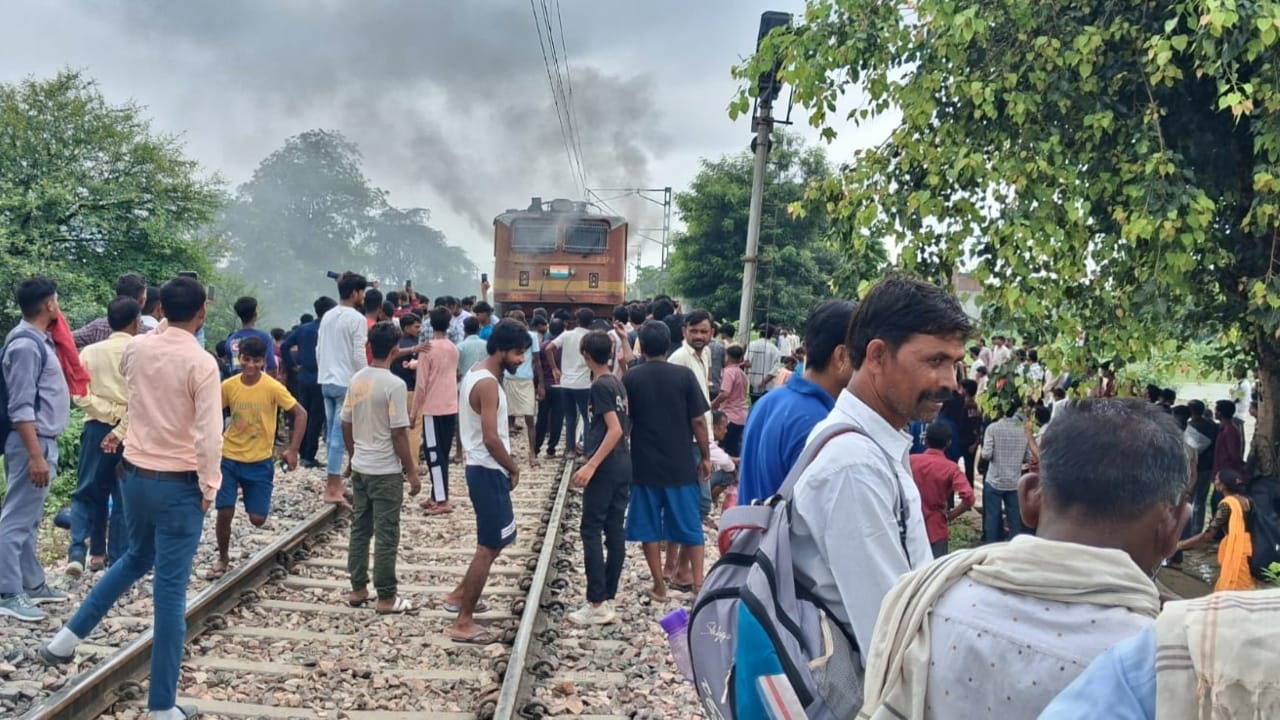 रेलवे ट्रैक पर यात्रियों की भीड़, ट्रेन के इंजन से निकलता धुआं