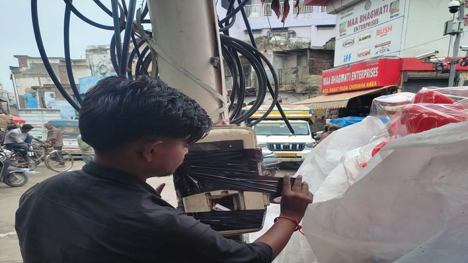 स्ट्रीट लाइट के पोल पर टेप लगाकर बोर्ड को सुरक्षित करता कर्मचारी