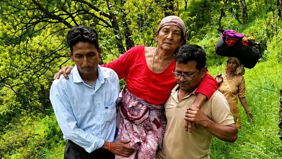 बीमार सरस्वती देवी को कंधे के सहारे पैदल सड़क तक ले जाते ग्रामीण।