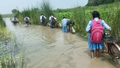 बाढ़ के पानी में होकर स्कूल जाते छात्र।