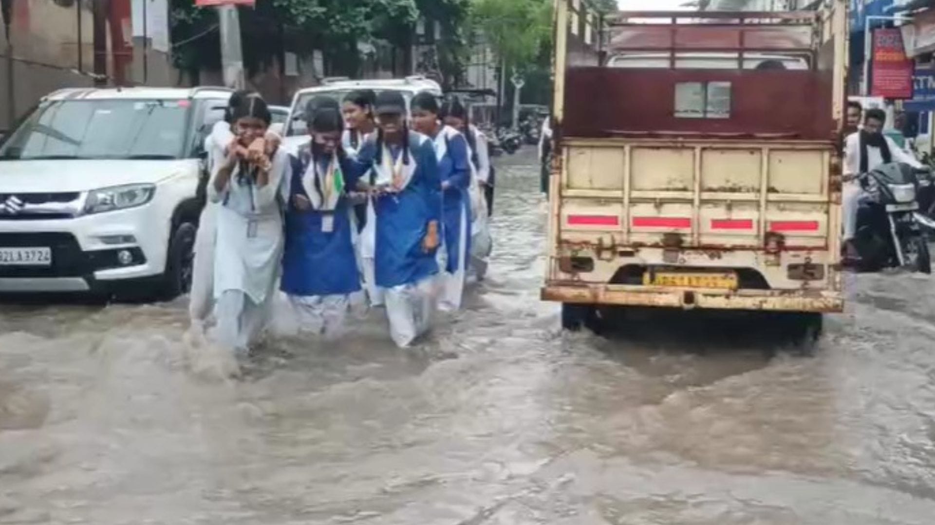 भारी बारिश के बाद जलभराव के बीच जाती छात्राएं और वाहन।