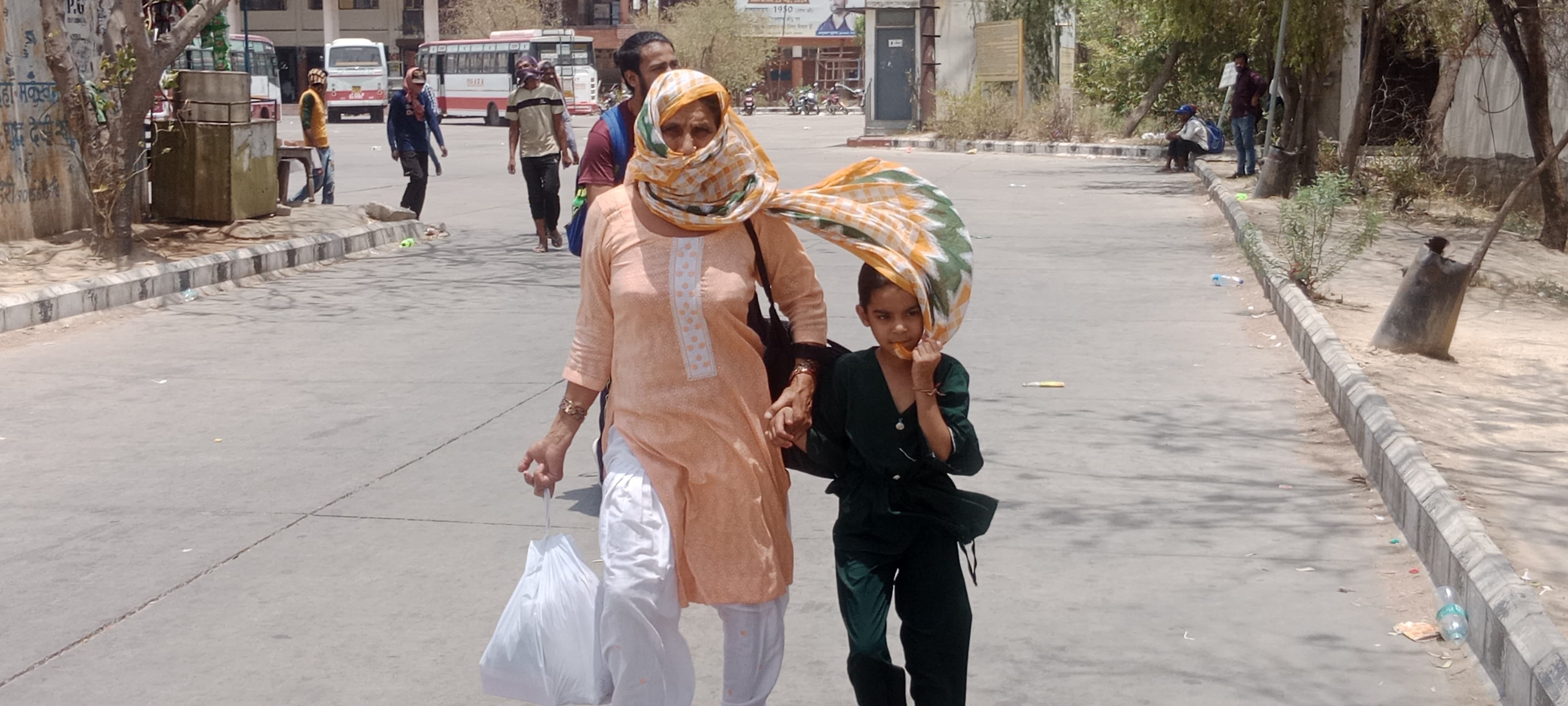 अपने बच्चे को गर्मी से बचाने के लिए दुपट्टे से बचाव कर लेकर जातीं महिला।