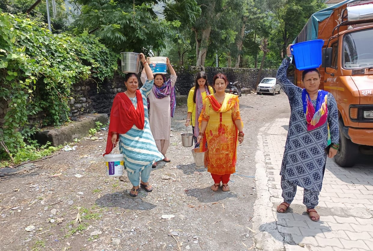 Women carrying utensils on their heads and bringing water from a hand pump two kilometers away.
