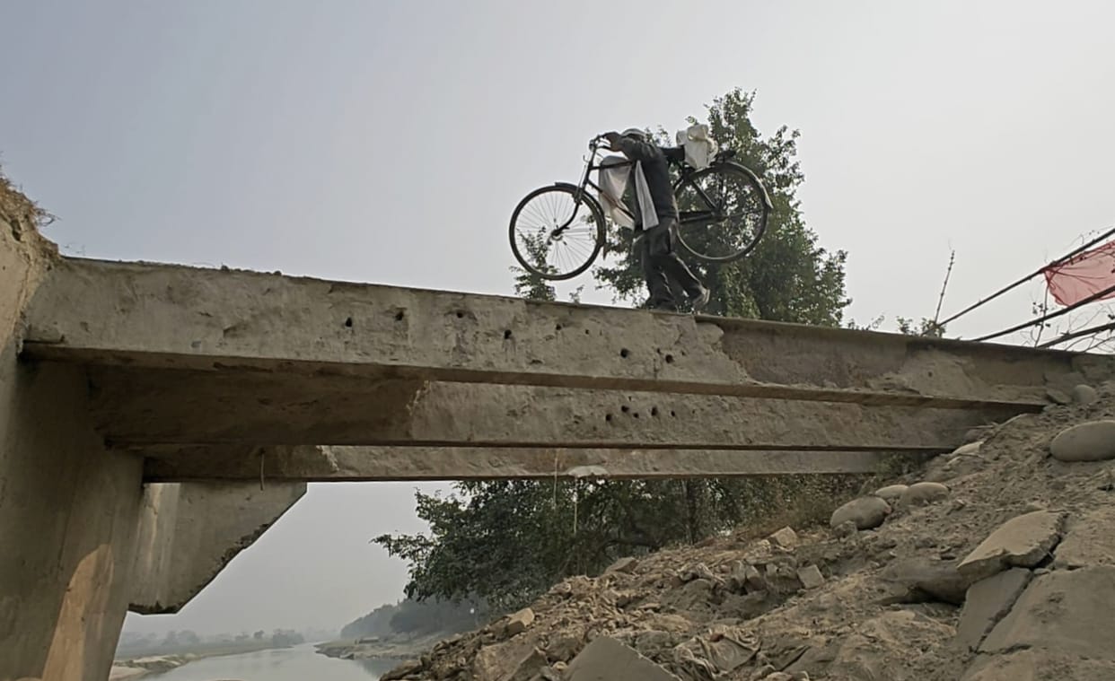 People cross the broken bridge carrying their bicycles on their shoulders