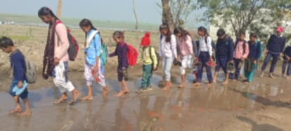 नौहझील में हाथ में जूते-चप्पल लेकर कीचड़ से  गुजरते बच्चे।