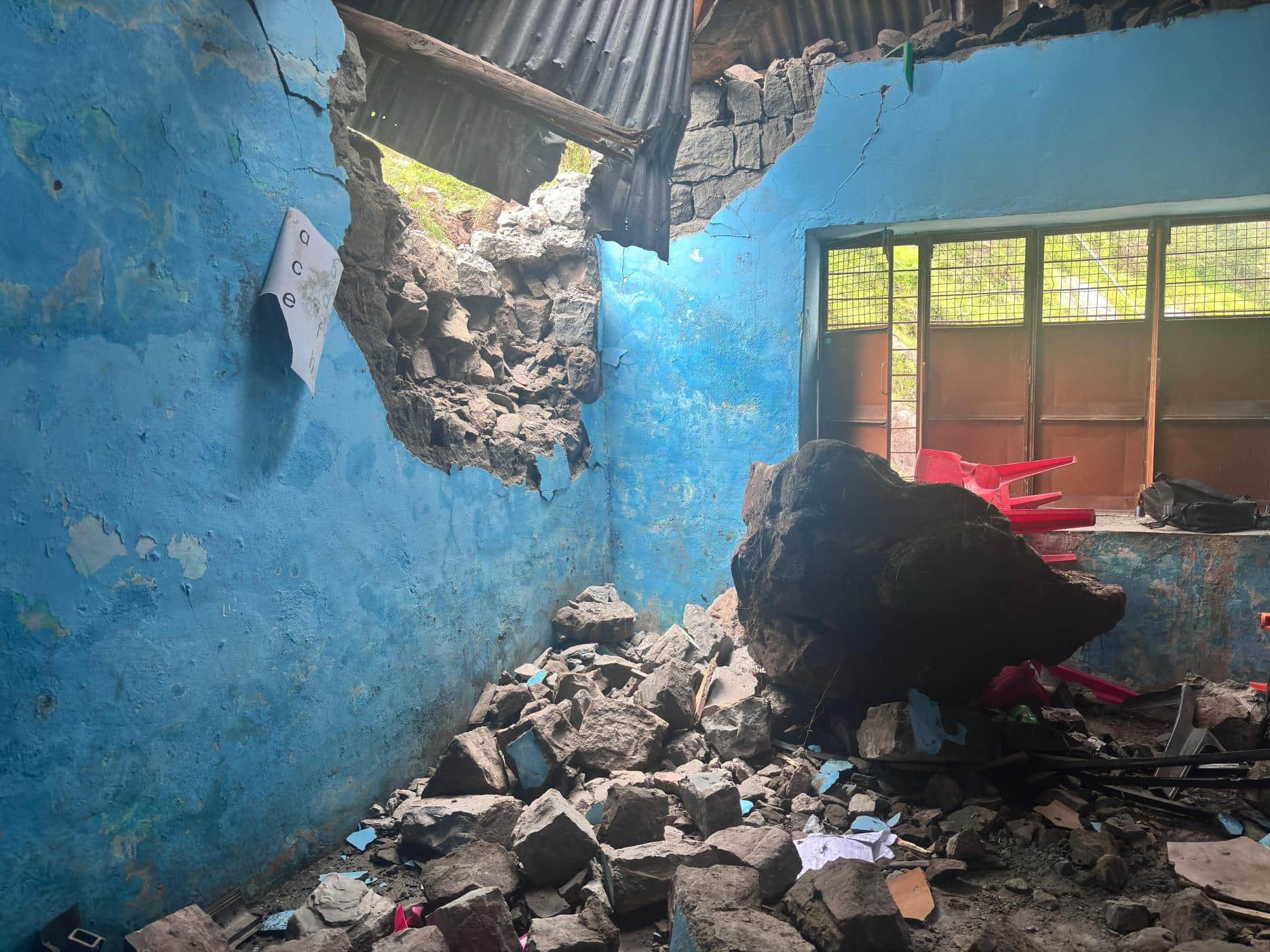 स्कूल की दीवार फाड़कर अंदर गिरा पत्थर। 