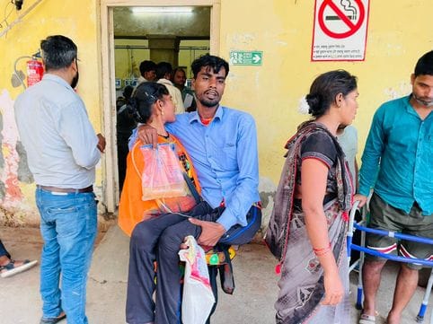 No wheelchair for the disabled woman reached with her husband in her lap