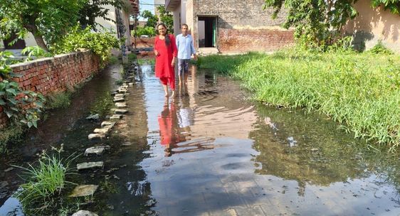 फोटो 36: सोनीपत के खरखौदा शहर में घरों के आगे गली में भरे पानी से गुजरते स्थानीय लोग। स्रोत: पा