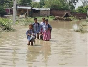 Knee-deep water, shoes in hand, difficult to reach school in flood