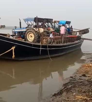 Due to the absence of a bridge, farmers are crossing the river by loading their tractors on boats.