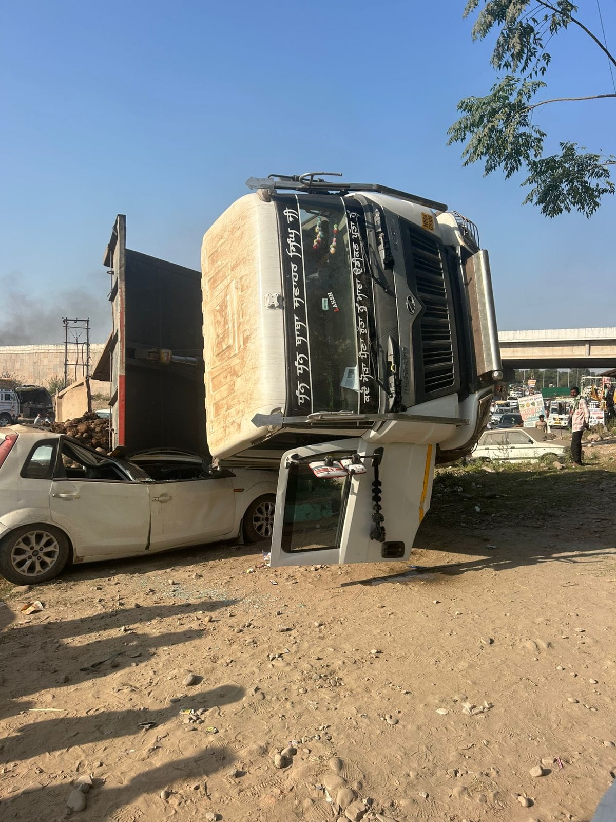 A truck full of debris overturned on the Surajpur bypass, trapping a car underneath.