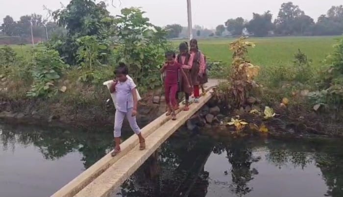 Children go to school by crossing the pole placed over the drain.