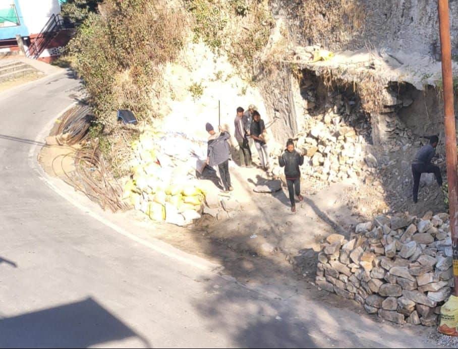 डीडीहाट में सड़क किनारे लगी लोनिवि की दीवार को ढहाते अतिक्रमणकारी। स्रोत: प्रशासन