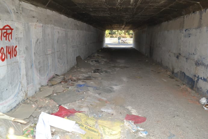 The underpass is not well lit and the road is in good condition, with open drains.