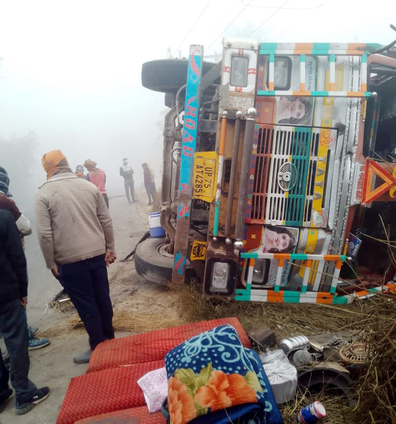 A truck loaded with corn overturned in dense fog; the driver and helper were injured.