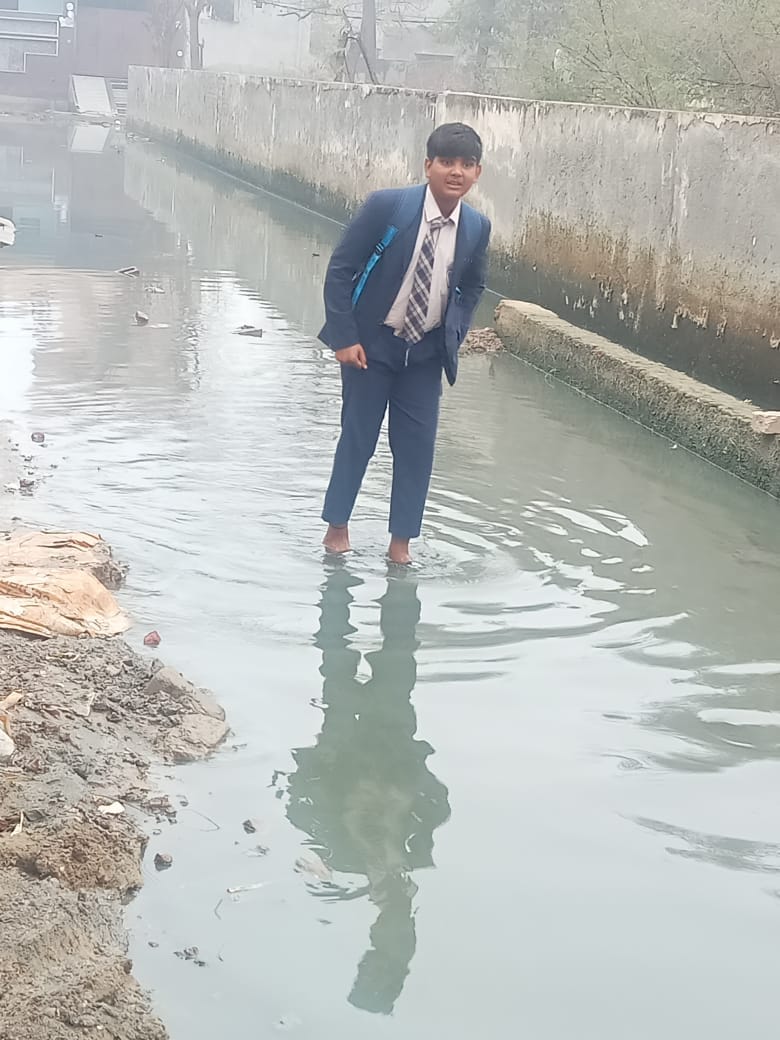 The street in Ward 8 is flooded with water, and children are wading through the dirty water to get to school.