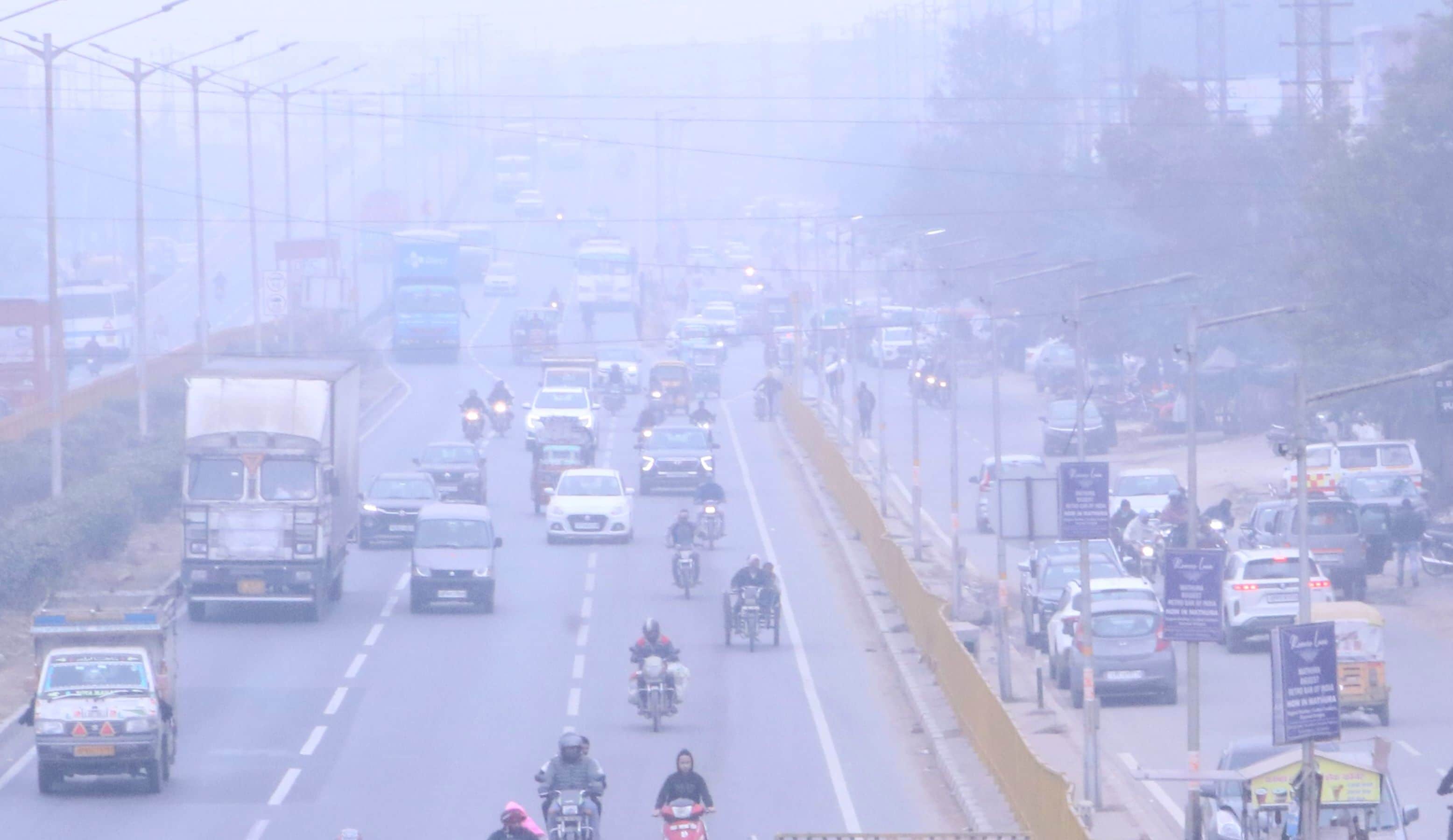 दोपहर में कोहरे की धुंध के बीच हाइवे से होकर गुजरते वाहन।