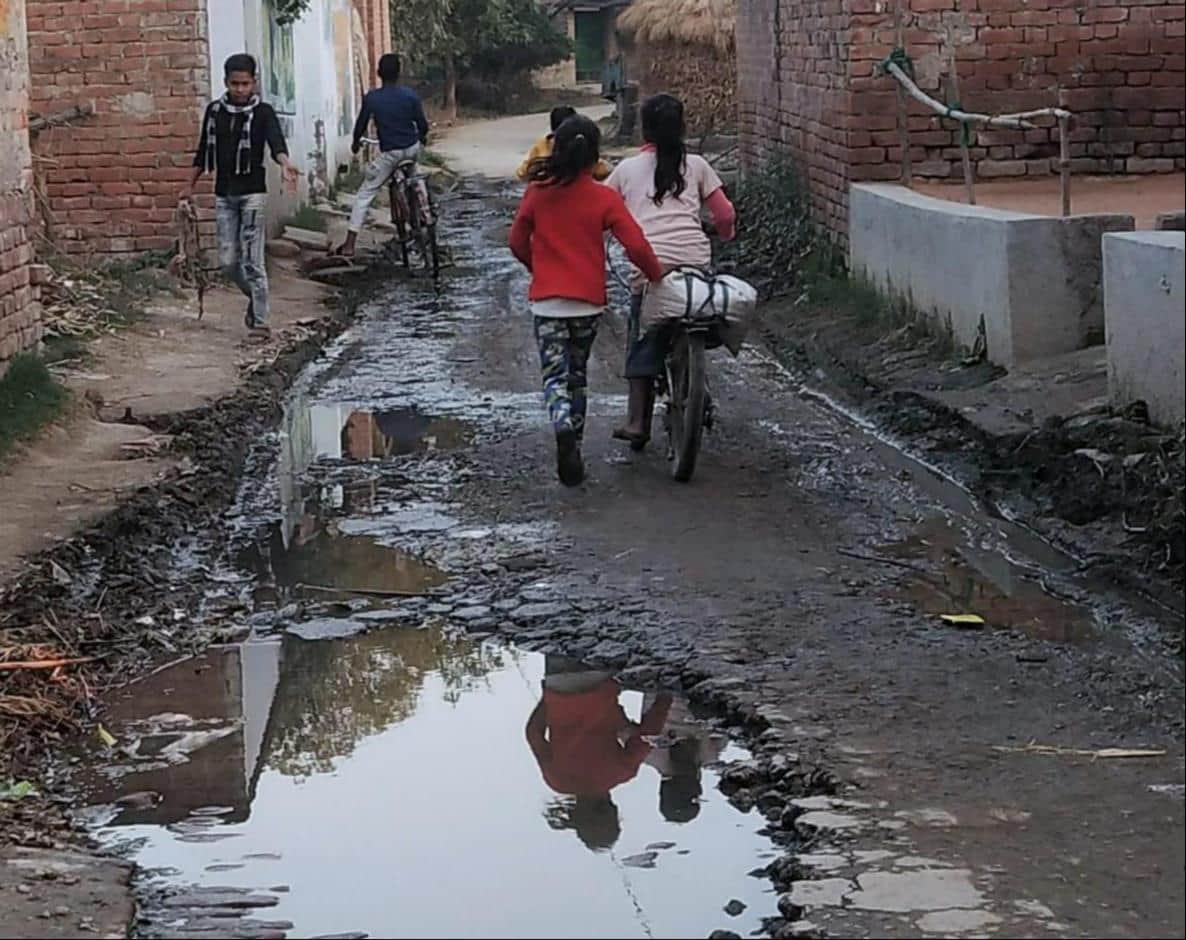 फोटो-9- भिखारीपुर पतसिया गांव में सड़क पर भरे कीचड़ के बीच से निकलते बच्चे। संवाद