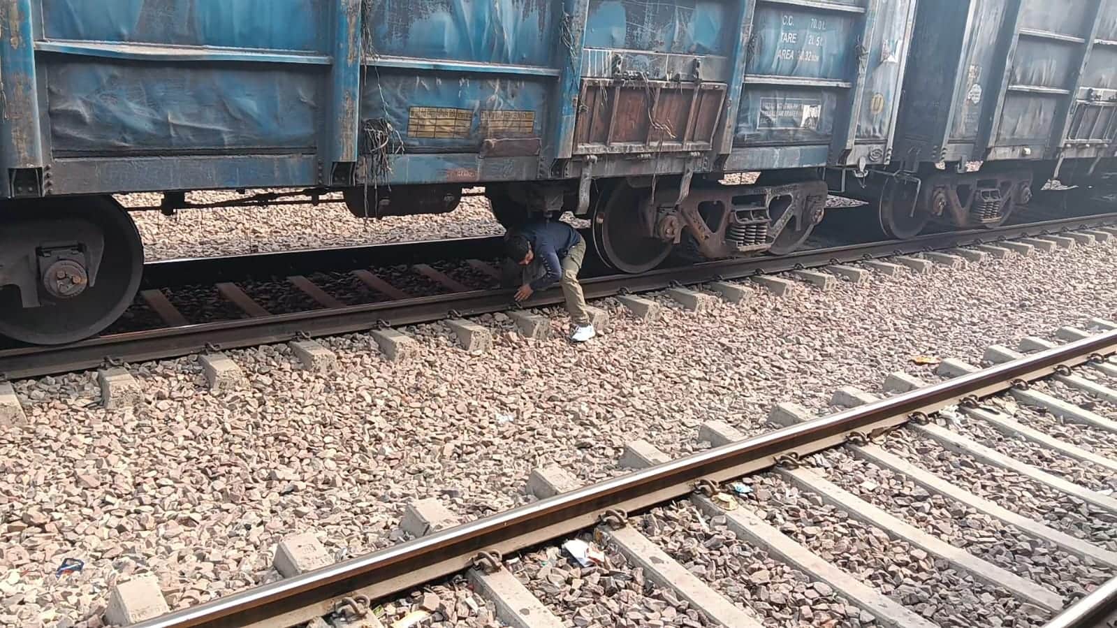 रेलवे स्टेशन पर ट्रैक पर खड़ी ट्रेन के नीचे से गुजरते लोग। 