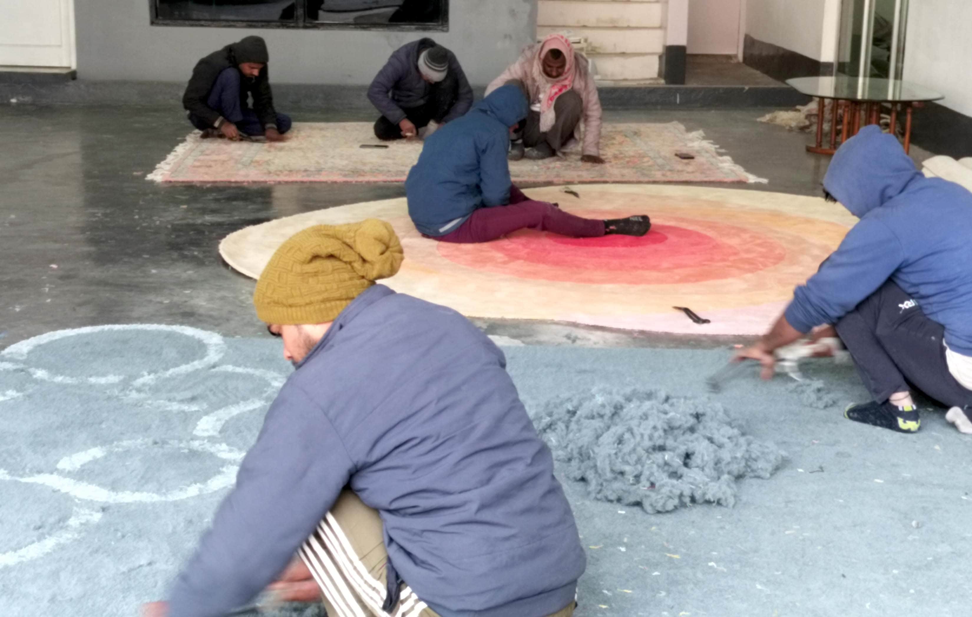 एक कालीन प्रतिष्ठान में कालीनों को अंतिम टच देते कारीगर। स्रोत-संवाद