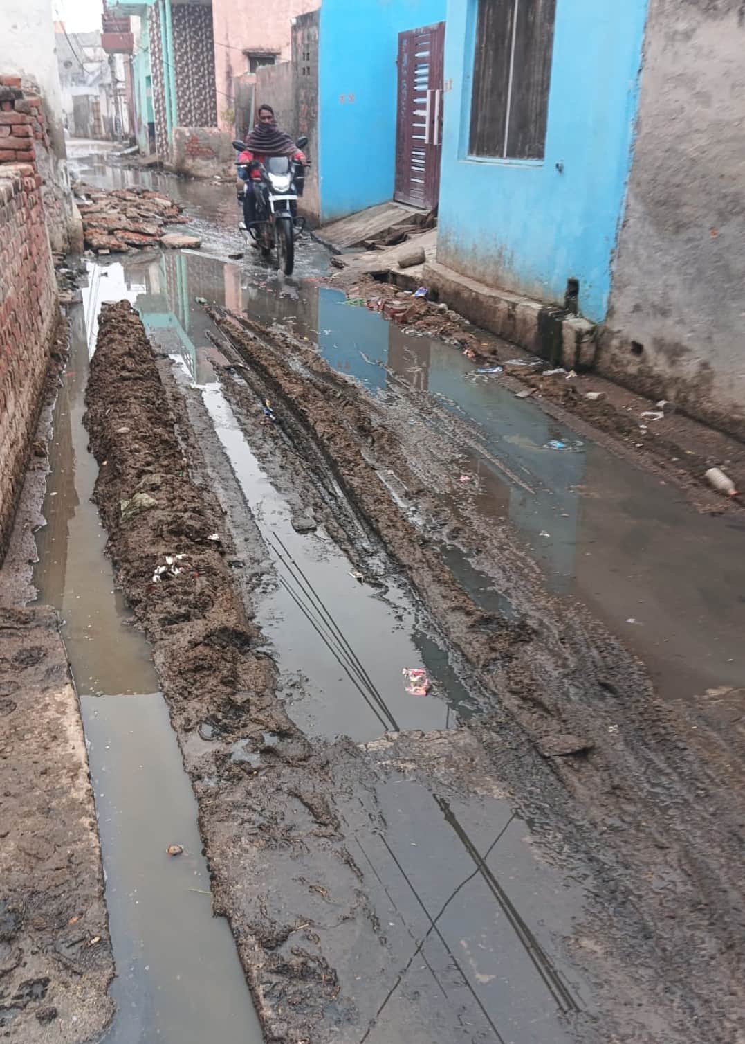 -फोटो 80 : आसौदा गांव की गलियों में जमा कीचड़ और निकलते दुपहिया चालक। संवाद