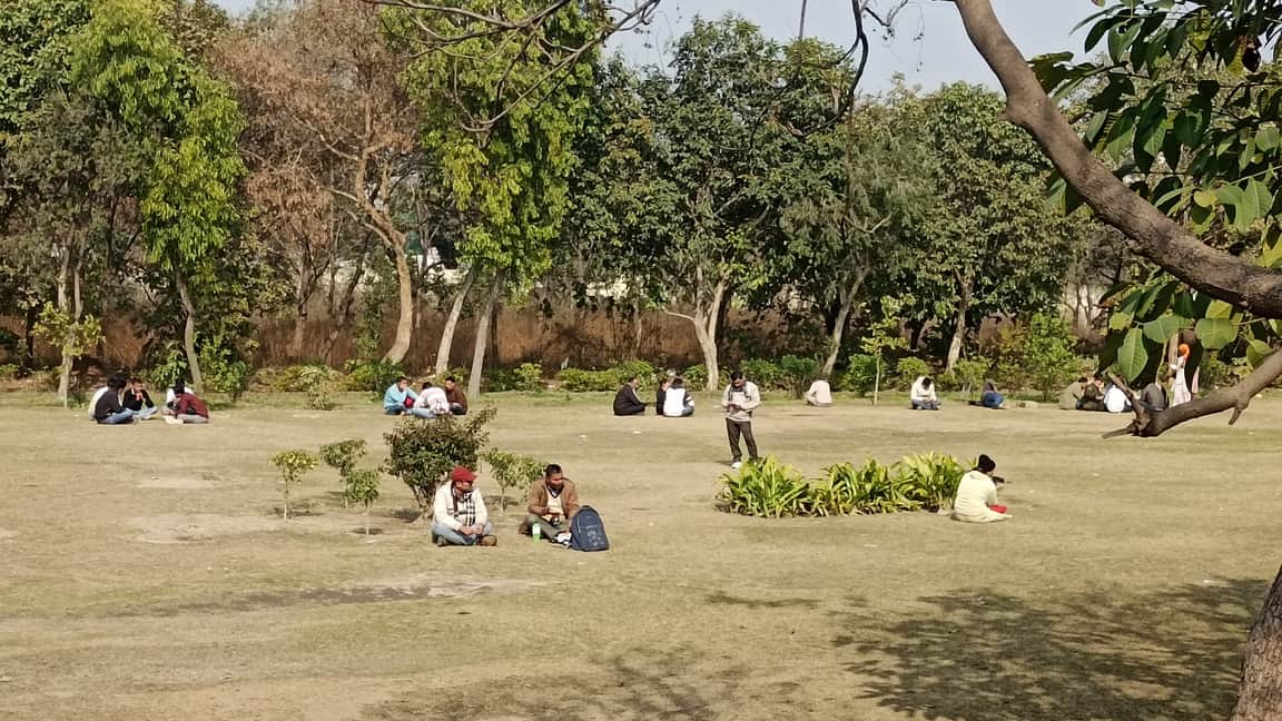 जिला सचिवालय के पार्क में दोपहर के समय धूप में बैठे लोग। संवाद