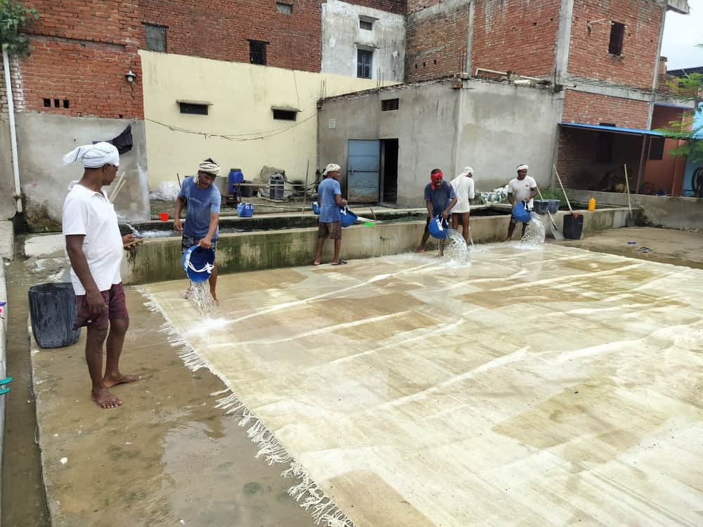 भदोही नगर के एक उत्पादन इकाई में कालीनों की धुलाई करते मजदूर। स्रोत- संवाद