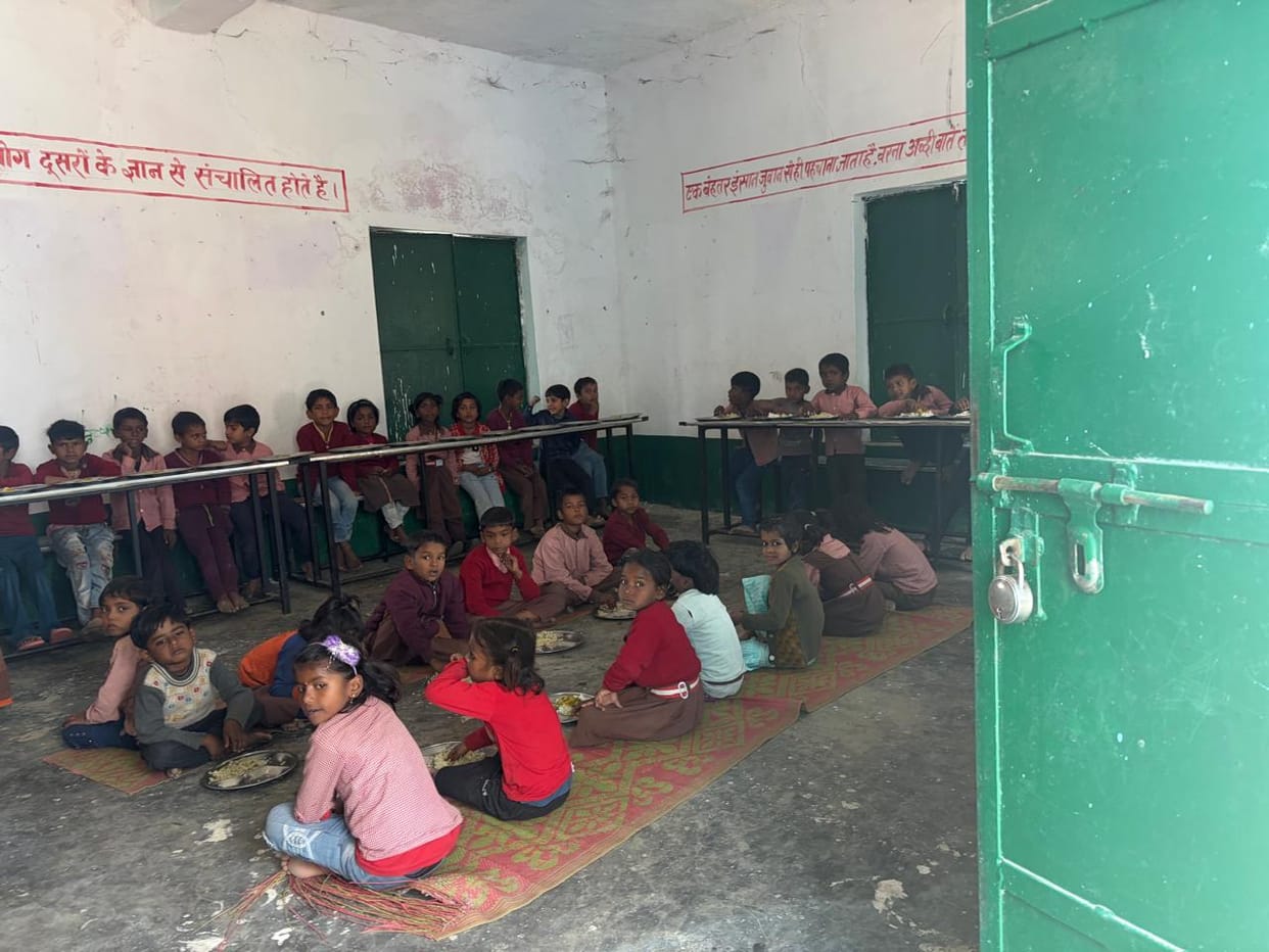Children sit on the floor and eat their meals