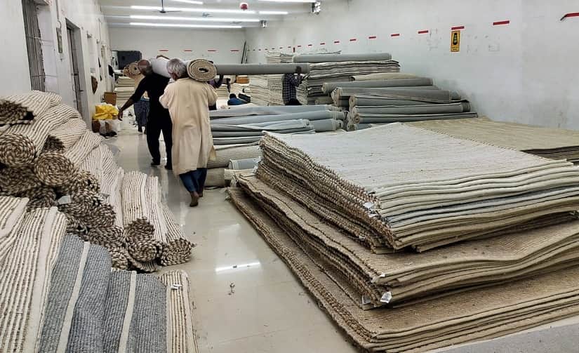 भदोही नगर के एक कालीन गोदाम में रखे कालीन और काम करते मजदूर। स्रोत- संवाद