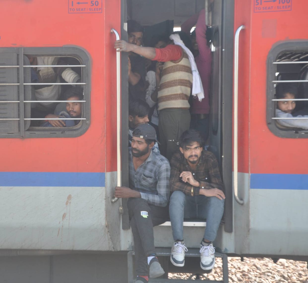 Passengers jostle in trains and buses, travelling by sitting at the door