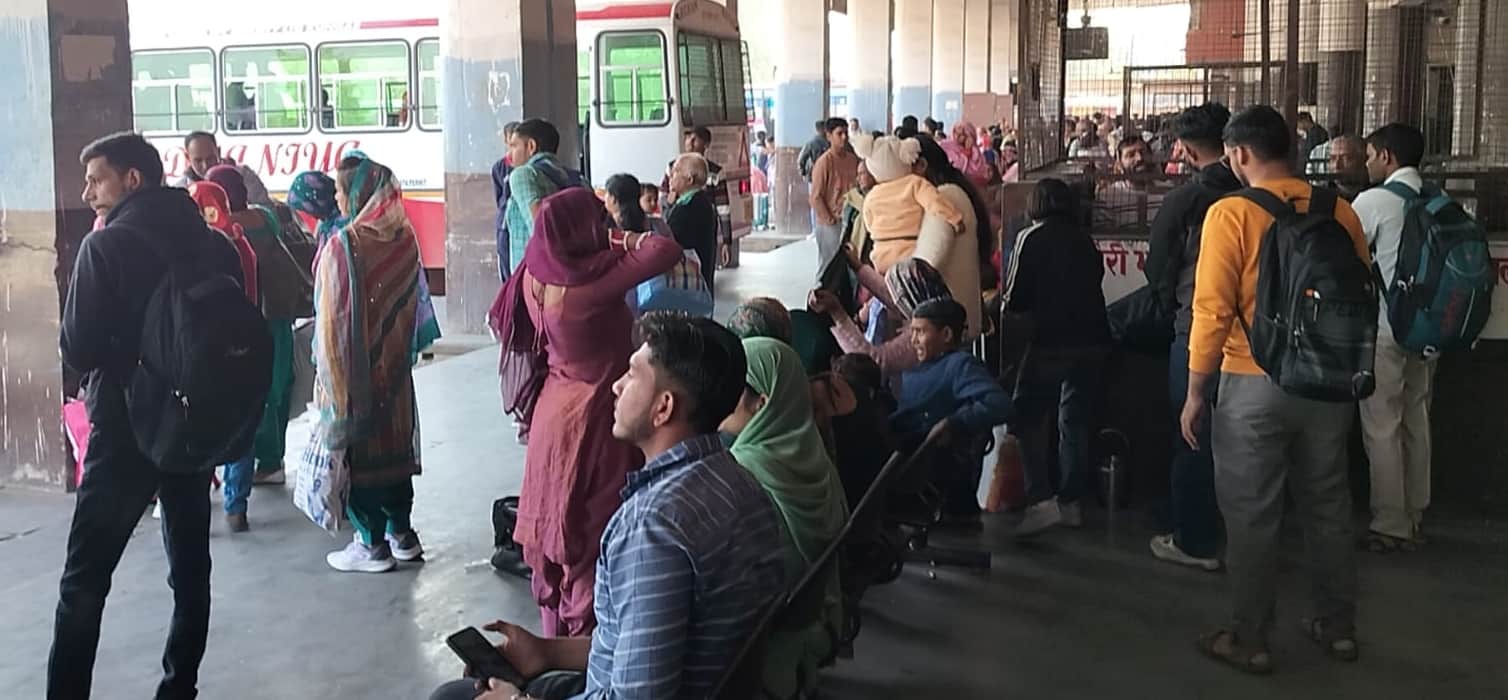 बस स्टैंड पर बसों का इंतजार करते यात्री।
