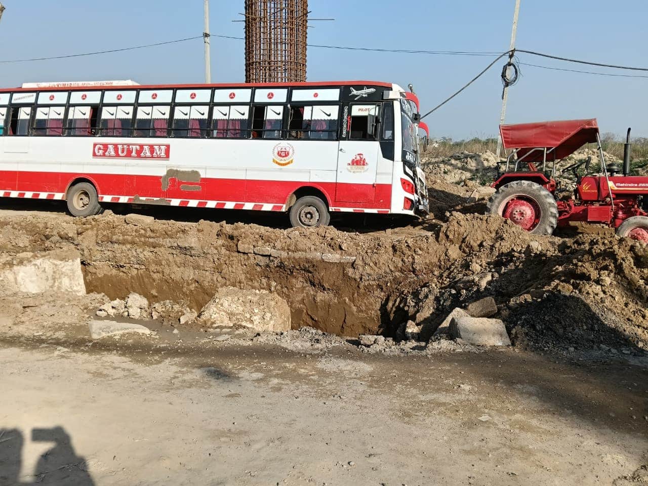 गड्ढे के पास धंसी परिवहन सिमिति की बस को निकालते हुए ट्रैक्टर।