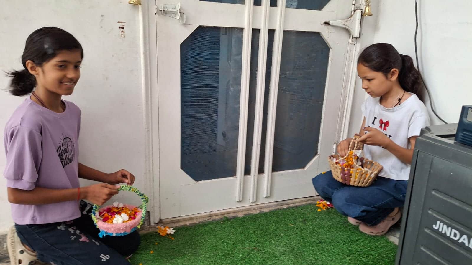 उग्रसेन नगर में दहलीज पर फूल बिखराते रीवा नेगी और गौरांगी। स्रोत जागरूक पाठक।