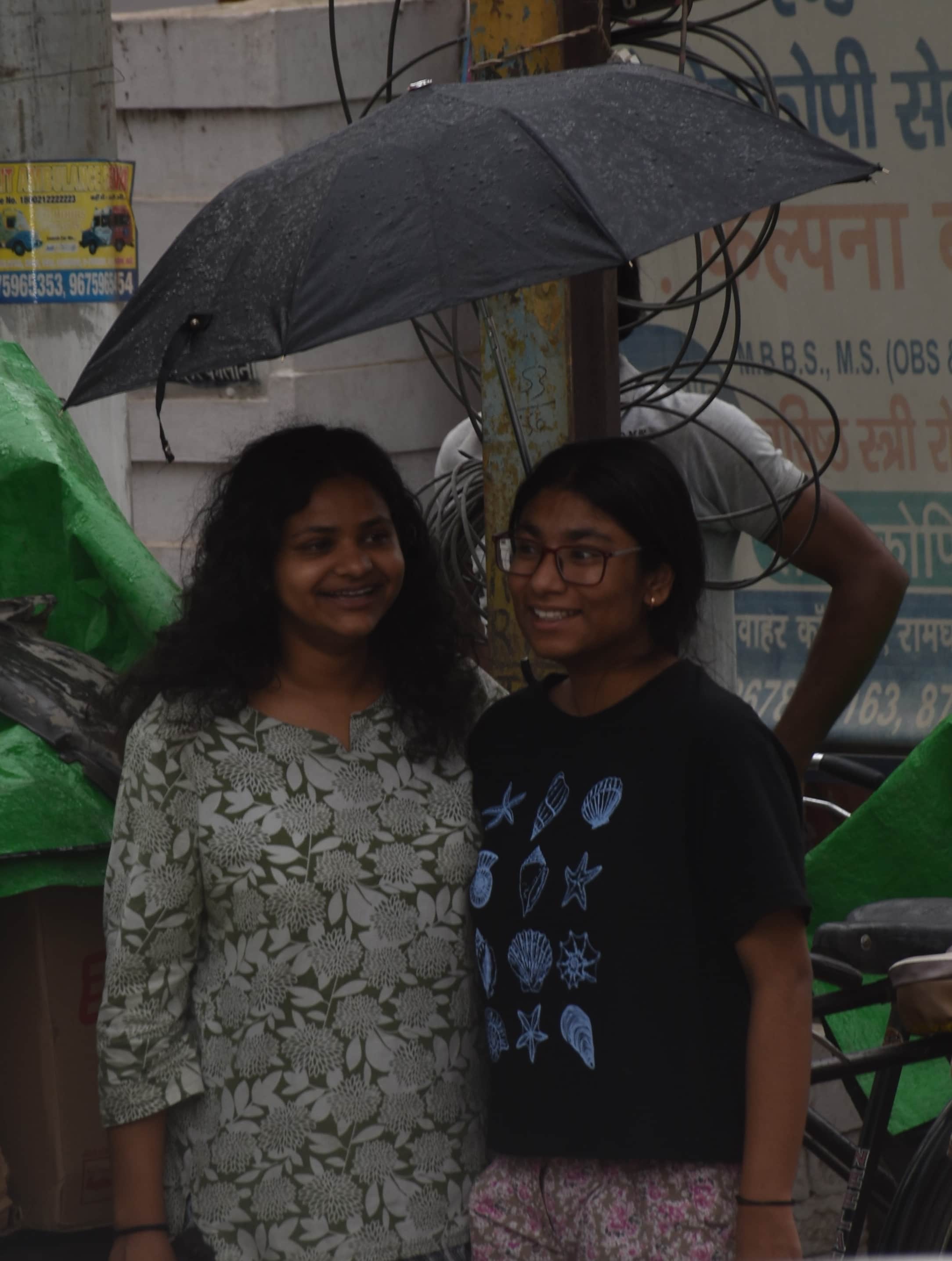 बूंदाबांदी होने पर छाता लगाकर जातीं युवतियां।