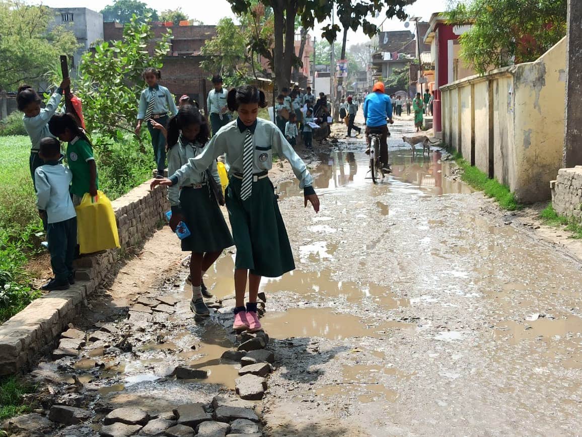 रामगढ़-बलिहार संपर्क मार्ग पर बह रहा नाबदान का पानी तथा बाउंड्री वॉल पर चढ़कर गुजरते स्कूली बच्