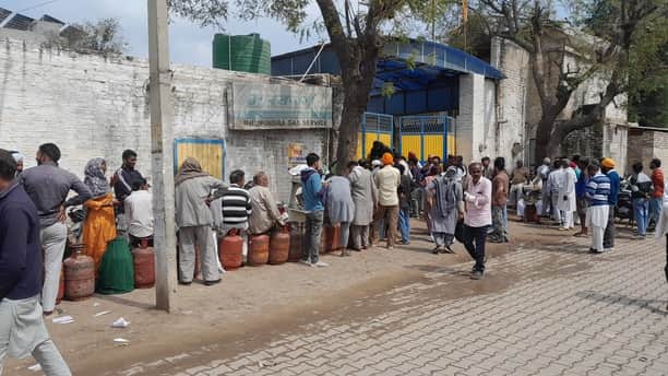 शहर की एक गैस एजेंसी के गोदाम के बाहर सिलिंडर के लिए कतार में खड़े उपभोक्ता। 