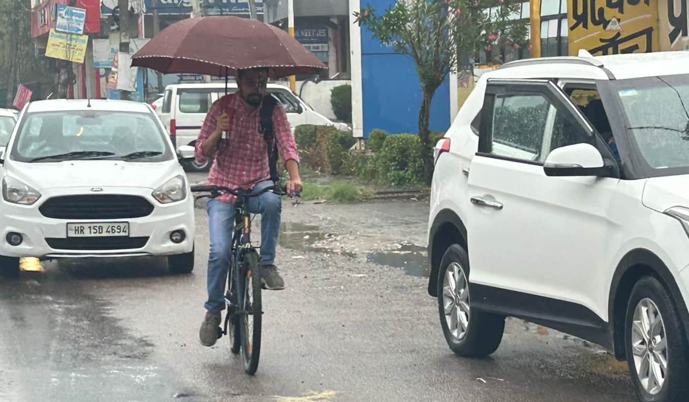 29-रोहतक के सोनीपत रोड पर बारिश के दौरान छाता लेकर जाता साइकिल सवार। संवाद
