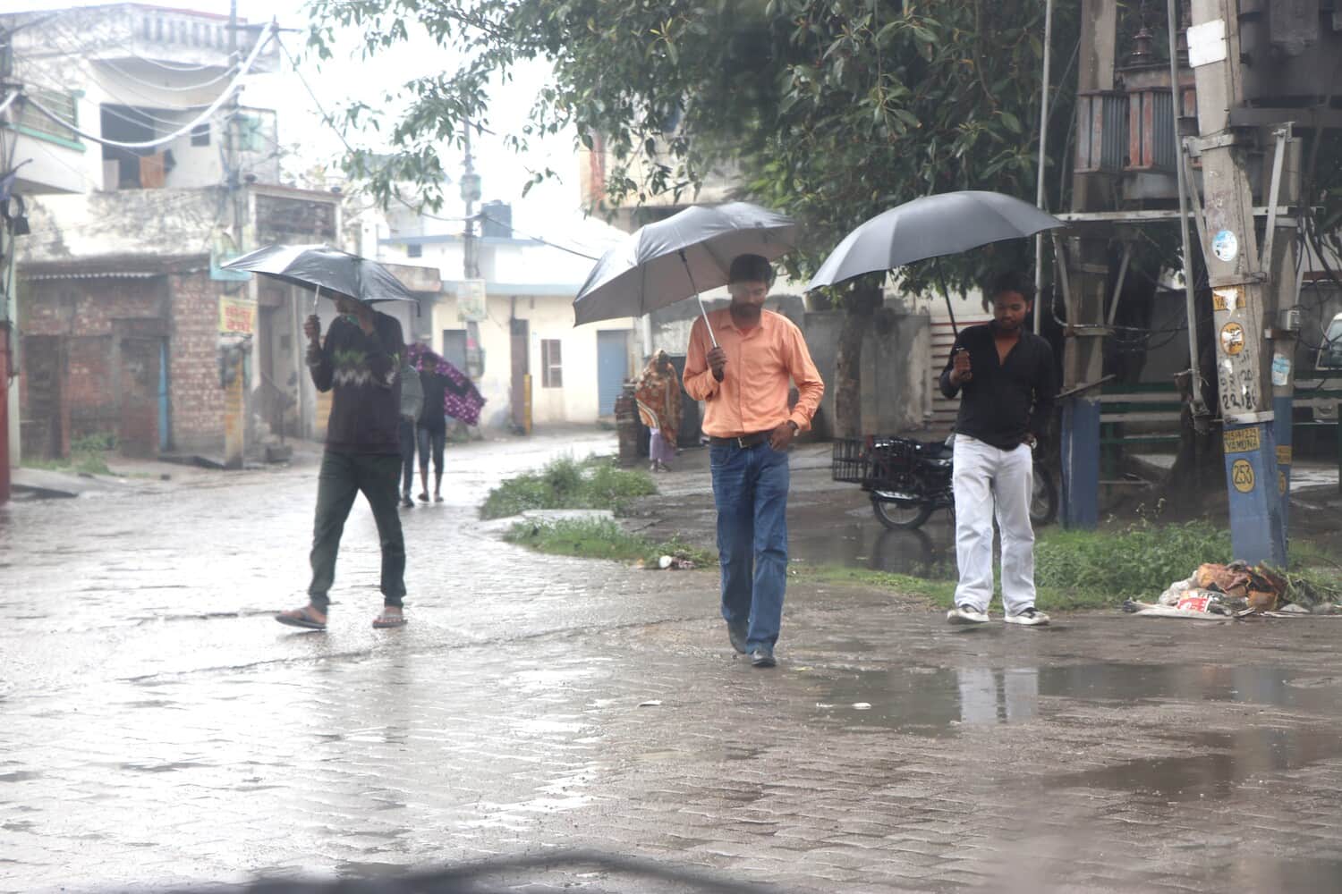 बारिश से बचने के लिए छाता लेकर गुजरते युवक। संवाद