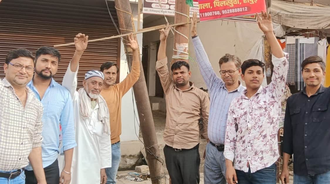 पिलखुवा के गांधी रोड पर जर्जर पोल के पास खड़े होकर प्रदर्शन करते लोग।स्रोत स्वयं