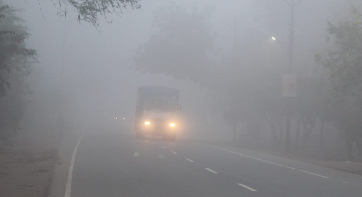 Dense fog blankets the area; vehicles seen crawling along the roads.