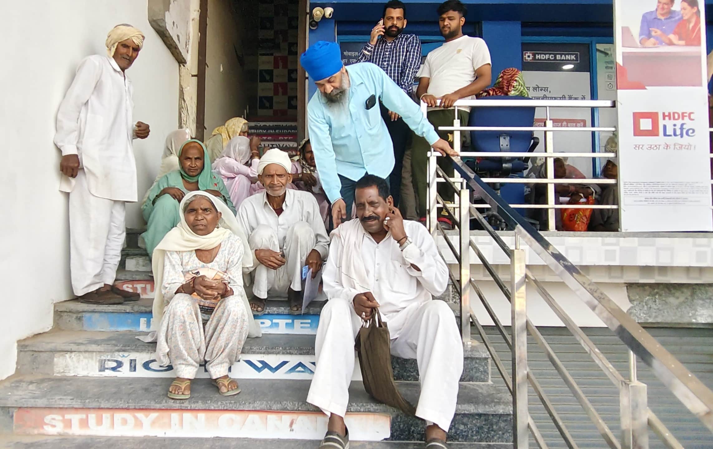  बैंक शाखा की सीढ़ियों पर बैठकर इंतजार करते बुजुर्ग। संवाद