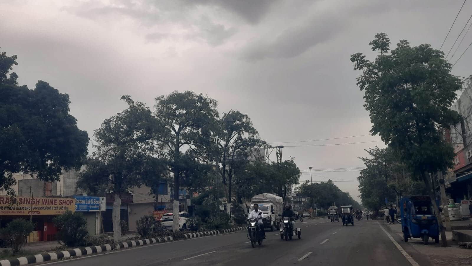 सुबह के समय बूंदाबांदी के दौरान रेलवे रोड से गुजरते लोग। संवाद