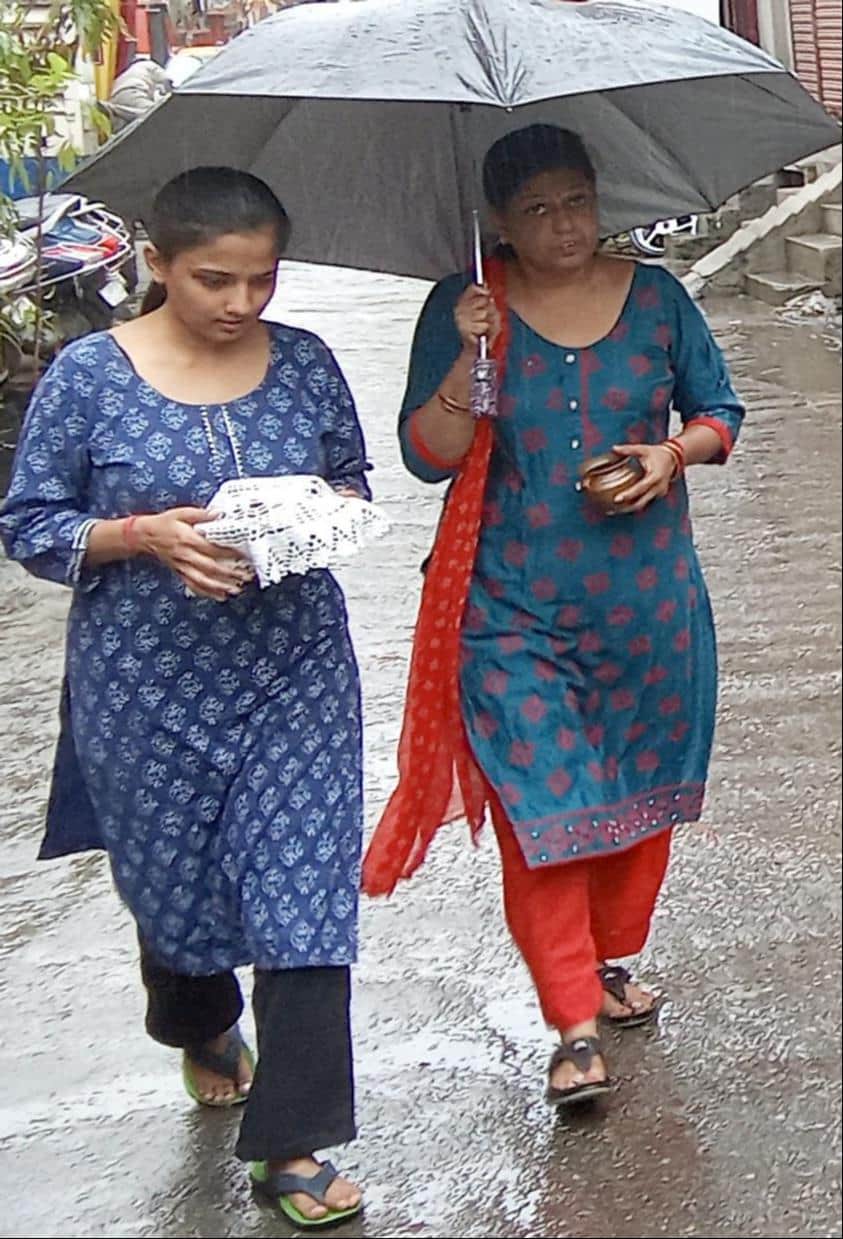 शामली  में बरसात के दौरान छाता लगा कर मंदिर जाती महिला और युवती । संवाद