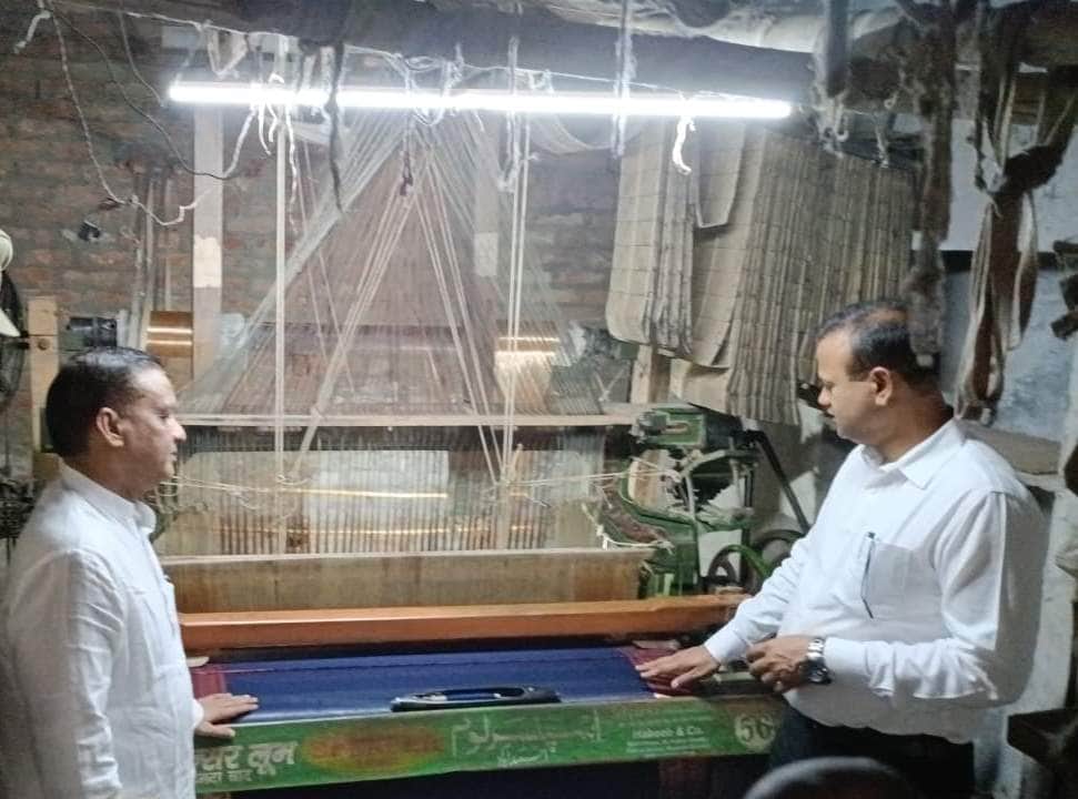 मुबारकपुर के कटरा में बुनाई कारखाना पर बुनी जा रही रेशमी साड़ी को देखते हुए डीएम रविंद्र कुमार।