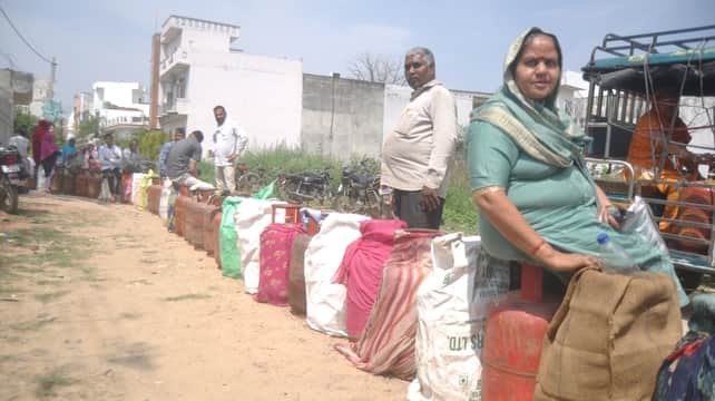 अपना घर कालोनी में गैस सिलिंडर लेने के लिए धूप में सिलिंडर पर बैठी महिला। संवाद