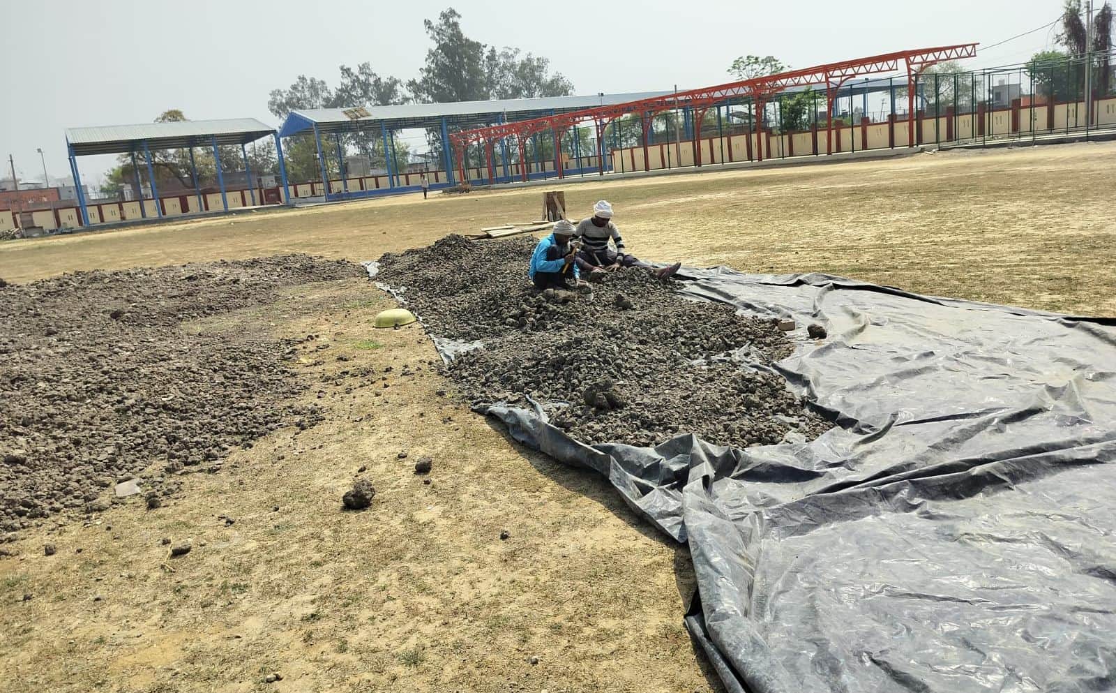 स्टेडियम में काली मिट्टी की पिच को तैयार करते मजदूर। संवाद