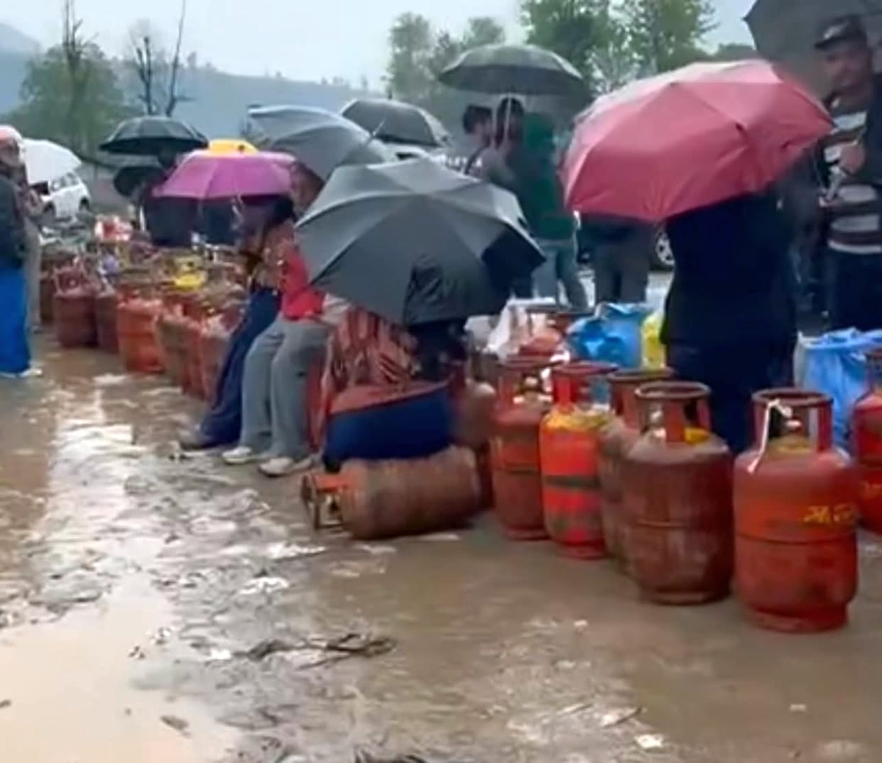 People waited for gas in the rain with umbrellas.