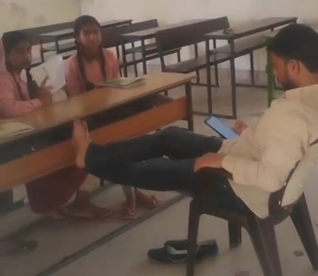 Video of a teacher watching his mobile with his feet propped up in front of children goes viral.