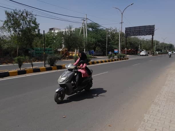 धूप से बचने के लिए सिर व चेहरे को ढककर जाती स्कूटी सवार युवती।