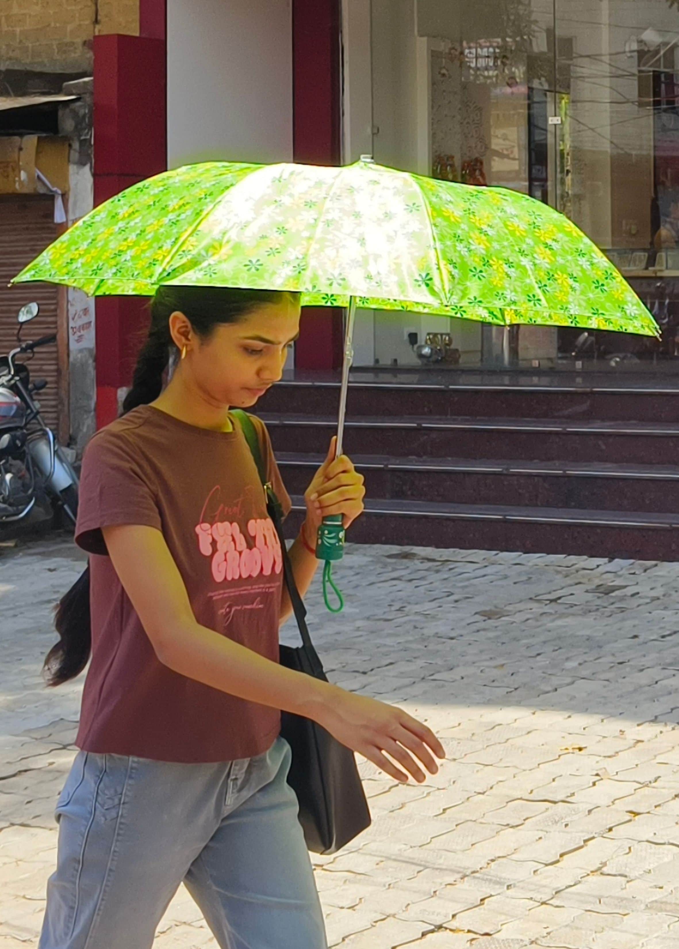 शहर में कचहरी रोड पर तेज धूप में छाता लगाकर जाती छात्रा। संवाद